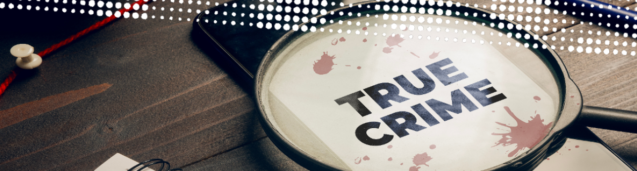 A magnifying glass on a wooden table focuses on the words "True Crime" with red splatters. Nearby are push pins and documents, creating a mysterious tone.