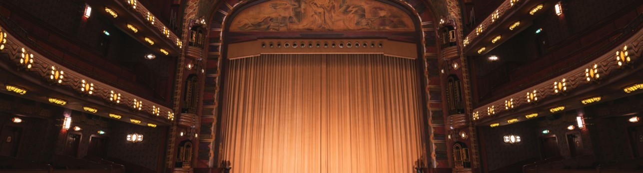 A theater interior featuring vibrant red seats and a grand curtain, creating an inviting atmosphere for performances.