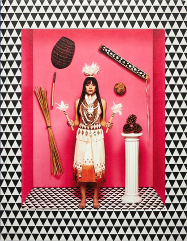 A woman in traditional attire stands against a pink background. She's flanked by cultural artifacts, pine cones on a pedestal, conveying a ceremonial tone.