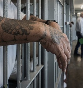 Man with Tattoos hanging arms over prison cell bars