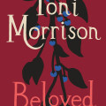Book cover for Toni Morrison’s *Beloved*: cream and pink lettering over a deep red background, with a dark branch and blue berries; notes her Nobel Prize.