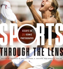 Sports Through the Lens: Essays on 25 Iconic Photographs A woman athlete celebrates passionately on a field, holding her jersey in the air. The cover of a book titled "Sports Through the Lens" overlays the image.